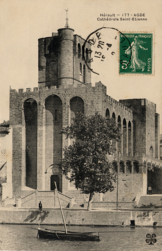 Carte postale ancienne légendée : Hérault - Agde - Cathédrale Saint-Étienne. La prise de vue est verticale On aperçoit l'Hérault 
au premier plan, une barque ancrée au milieu de l'eau, et en arierre plan, magestueuse, la Cathédrale Saint-Étienne entièrement 
construite de pierres de lave.