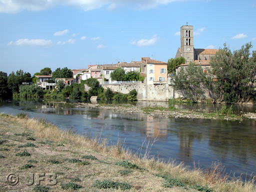 On aperçoit la rivière Aude, de couleur bleue à cette occasion, et sur les berges opposées, quelques maisons de Trèbes et l'église.