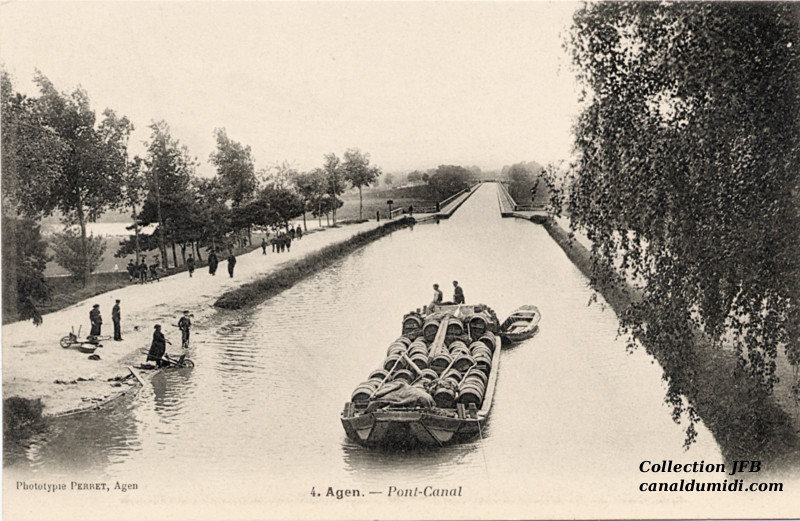 Carte postale ancienne du Canal des Deux Mers légendée : Agen, Pont-Canal: Vue de face du Pont-Canal sur la Garonne. Une péniche avec une cargaison de barriques tire une barque. Deux hommes sur la péniche. Sur les bords du Canal, des lavandières