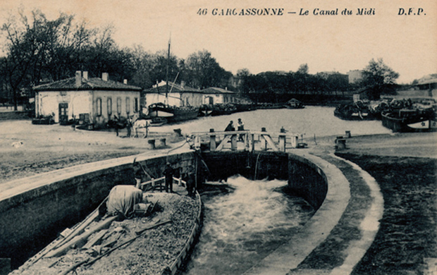 Vue d'ensemble du port de Carcassonne ; quelques péniches amarrées sur les quais ; une autre péniche halée par deux chevaux se prépare à accéder au port en passant l'écluse