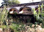 Trois arches de l'épanchoir vues en contre-plongée avec partie du tablier du pont-canal qui soutient l'ouvrage.