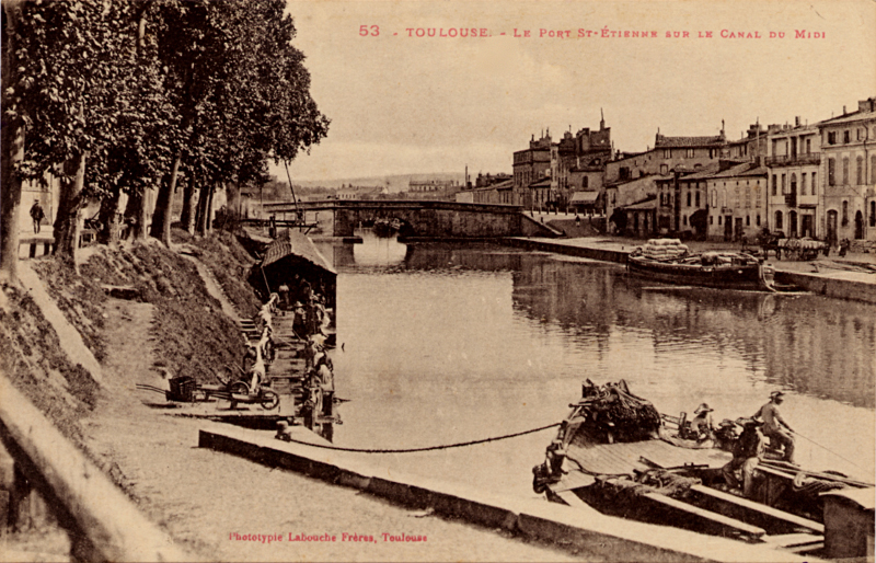 Carte postale ancienne légendée : Tousouse - Le port Saint Étienne sur le Canal du Midi. On aperçoit à gauche, le lavoir couvert, à droite une péniche. Au tout premier plan, sur une péniche, un pêcheur...